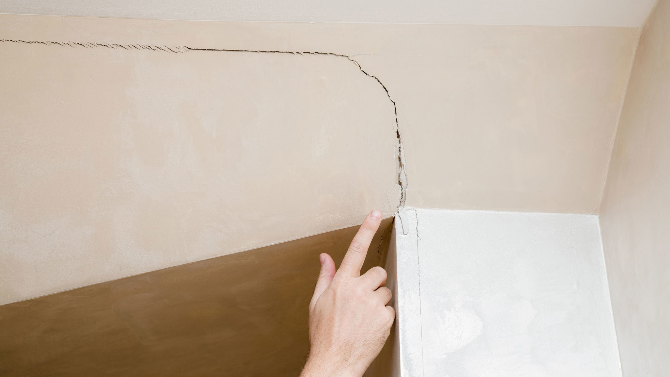 Hand pointing to crack in the wall caused by an earthquake.